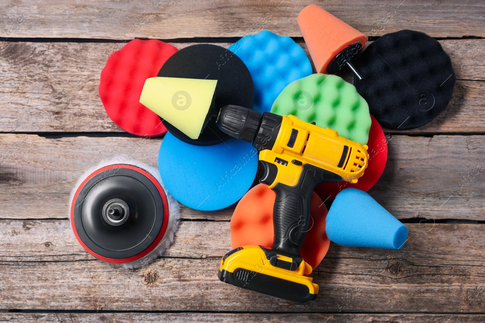 Photo of Electric screwdriver with different polish pads on wooden background, flat lay