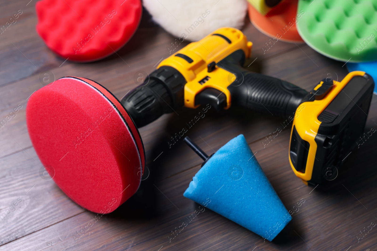 Photo of Electric screwdriver with different polish pads on wooden background, closeup