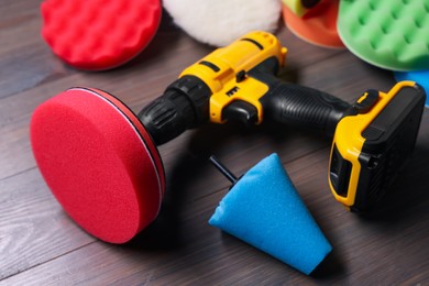 Photo of Electric screwdriver with different polish pads on wooden background, closeup