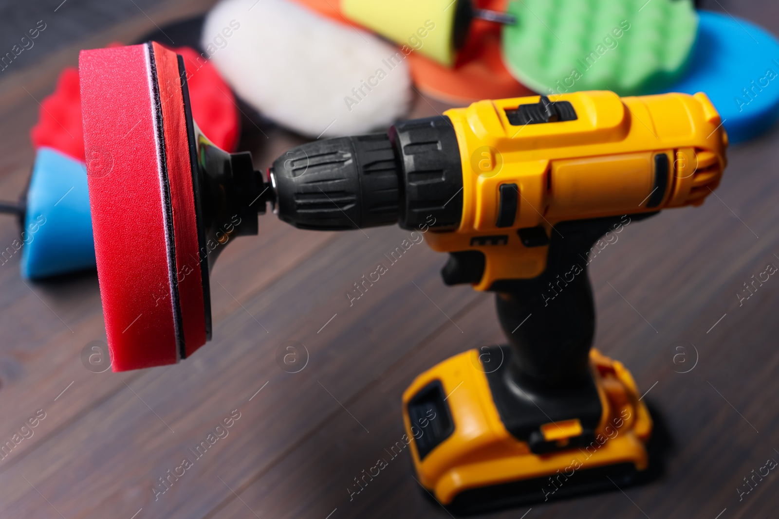 Photo of Electric screwdriver with different polish pads on wooden background, closeup