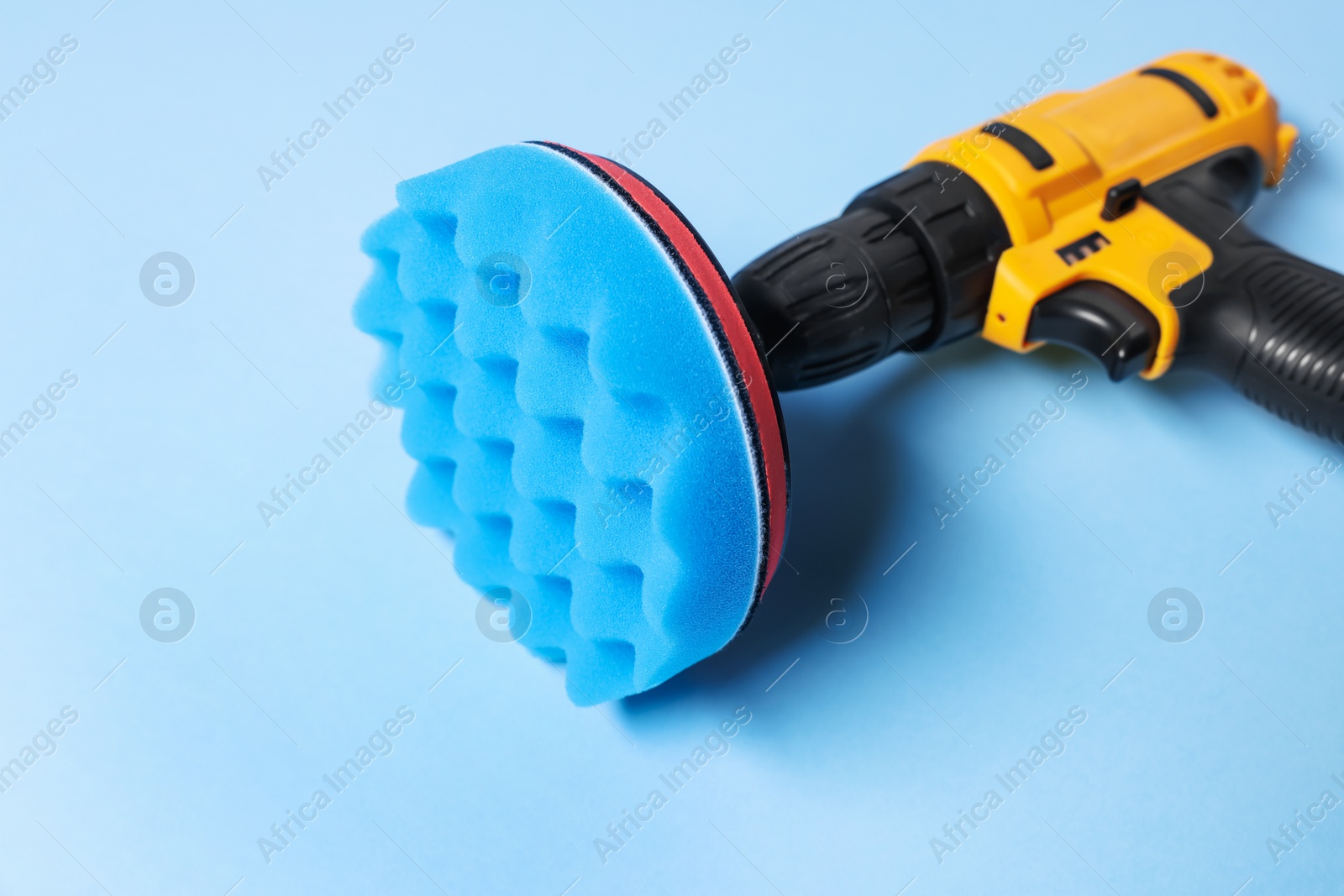 Photo of Electric screwdriver with polish pad on light blue background, closeup