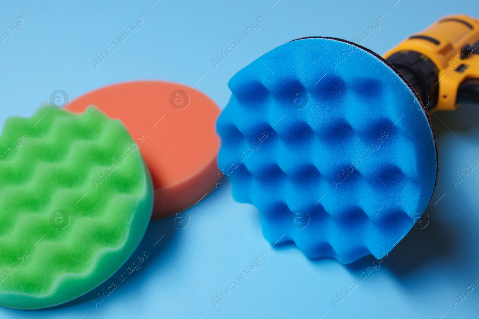 Photo of Electric screwdriver with different polish pads on light blue background, closeup