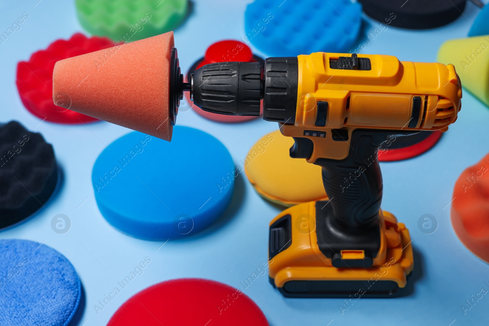 Photo of Electric screwdriver with different polish pads on light blue background, closeup