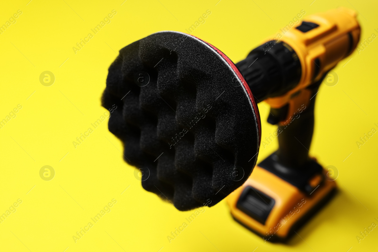 Photo of Electric screwdriver with polish pad on yellow background, closeup