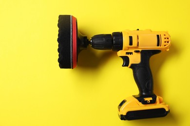 Photo of Electric screwdriver with polish pad on yellow background, top view