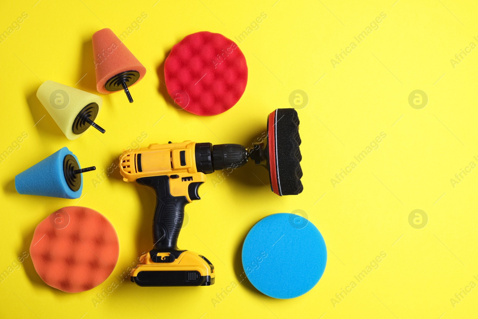 Photo of Electric screwdriver with different polish pads on yellow background, flat lay. Space for text