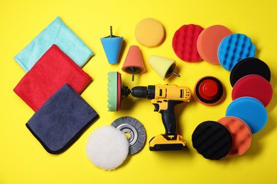 Photo of Electric screwdriver with different polish pads on yellow background, flat lay