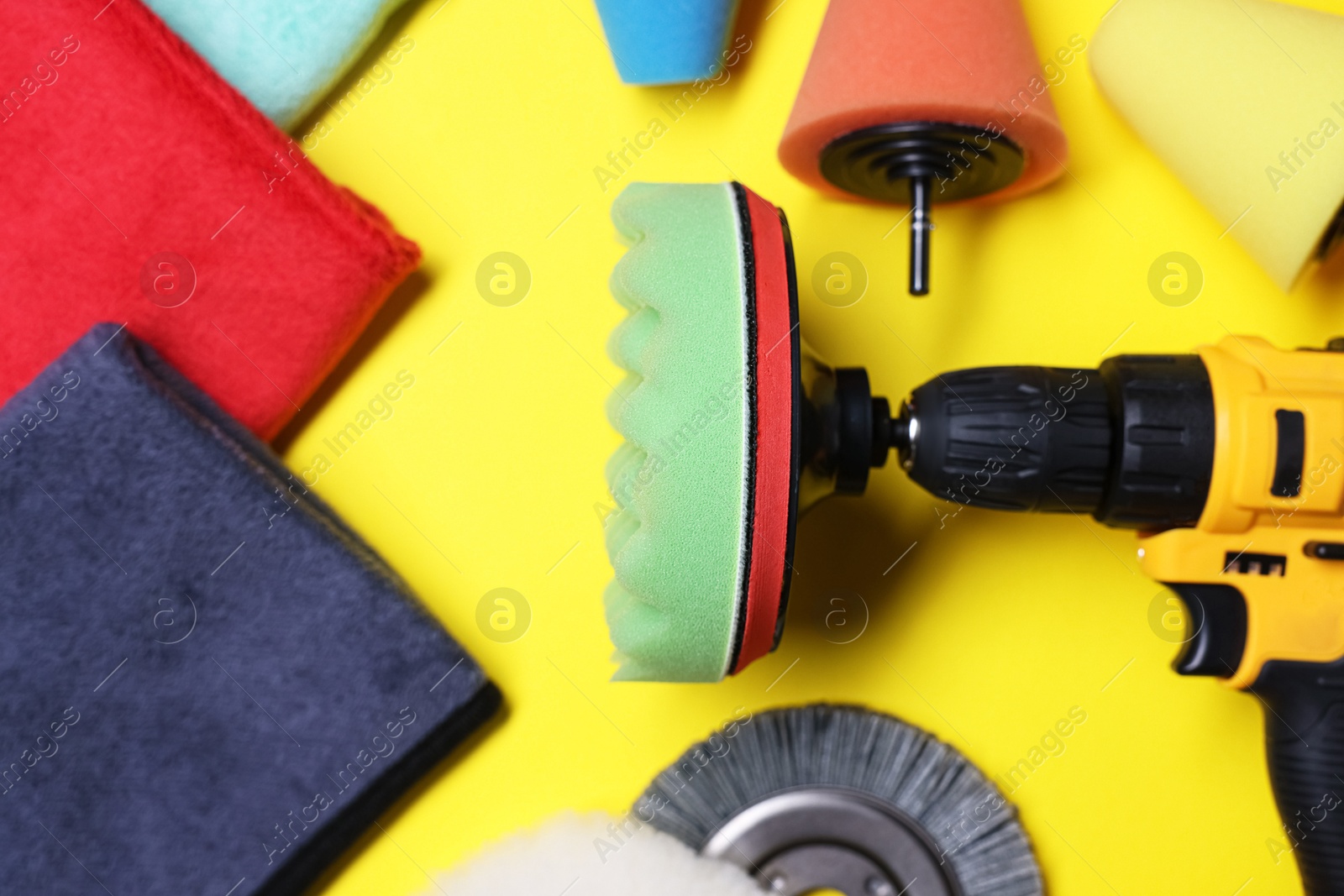 Photo of Electric screwdriver with different polish pads on yellow background, flat lay