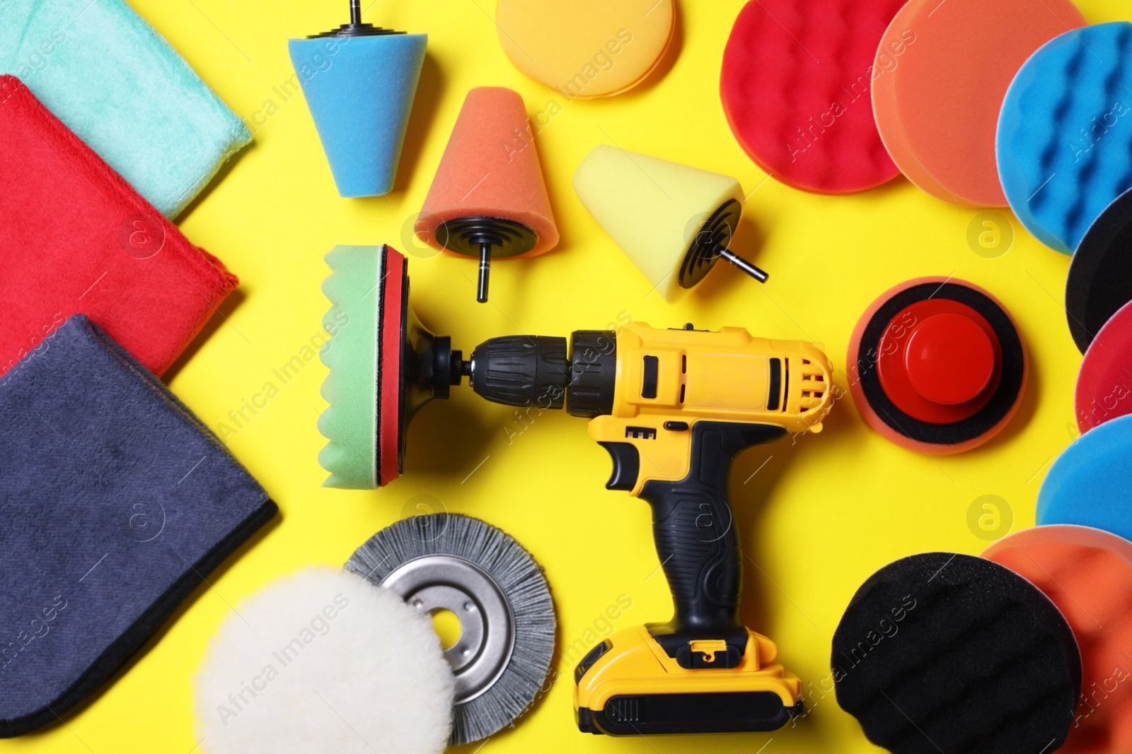 Photo of Electric screwdriver with different polish pads on yellow background, flat lay