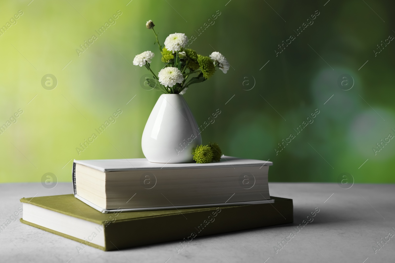 Photo of Books and vase with beautiful flowers on grey textured table against blurred green background, closeup