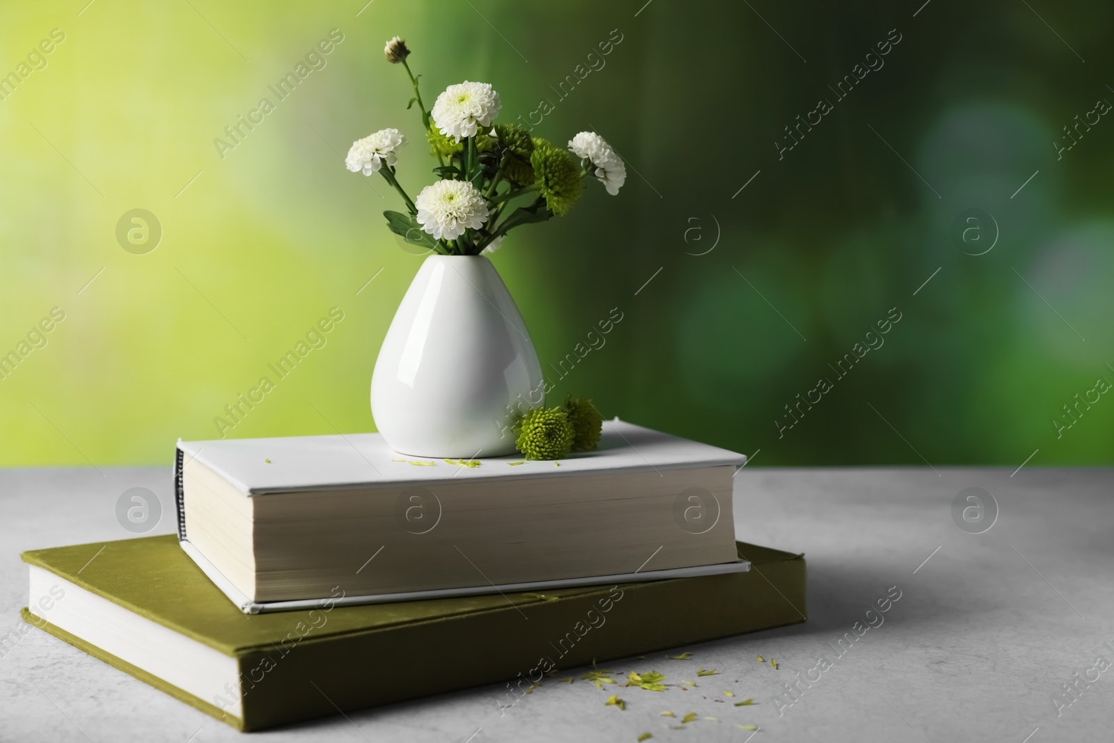 Photo of Books and vase with beautiful flowers on grey textured table against blurred green background, closeup