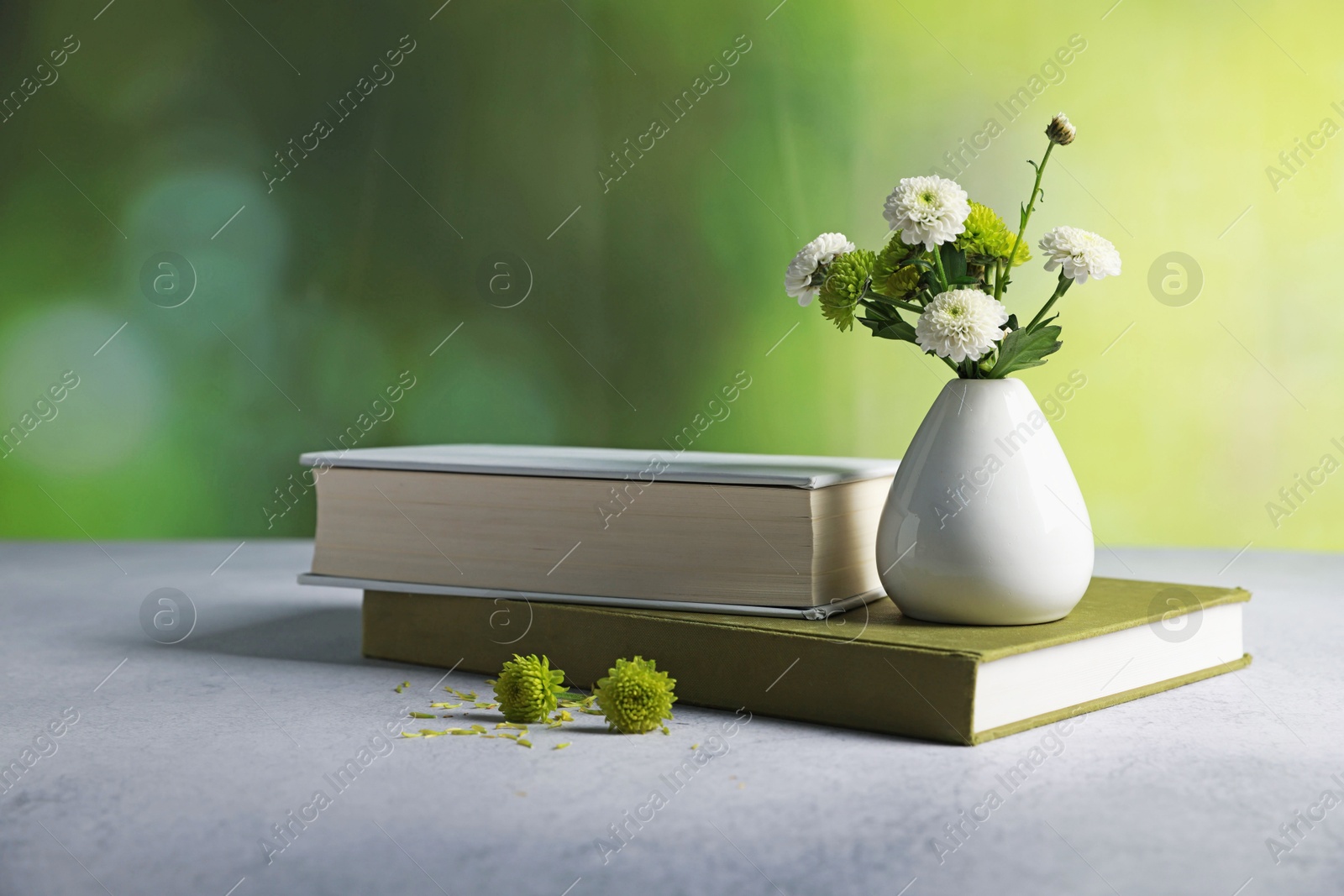 Photo of Books and vase with beautiful flowers on grey textured table against blurred green background, closeup