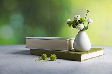 Photo of Books and vase with beautiful flowers on grey textured table against blurred green background, closeup