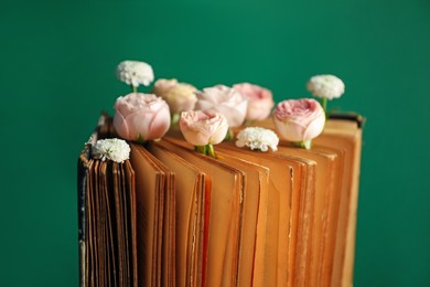 Photo of Book with beautiful flowers against green background, closeup