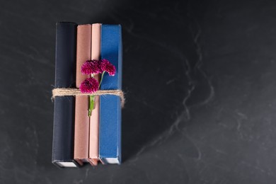 Books with beautiful flowers on dark textured table, top view. Space for text