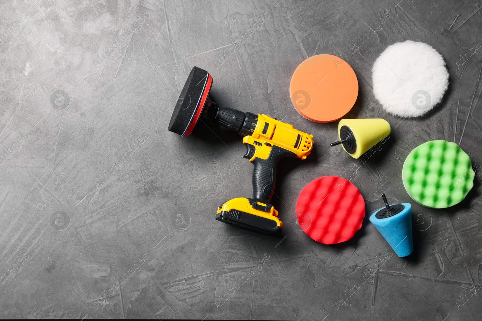 Photo of Different polish pads and electric screwdriver on grey textured table, flat lay. Space for text