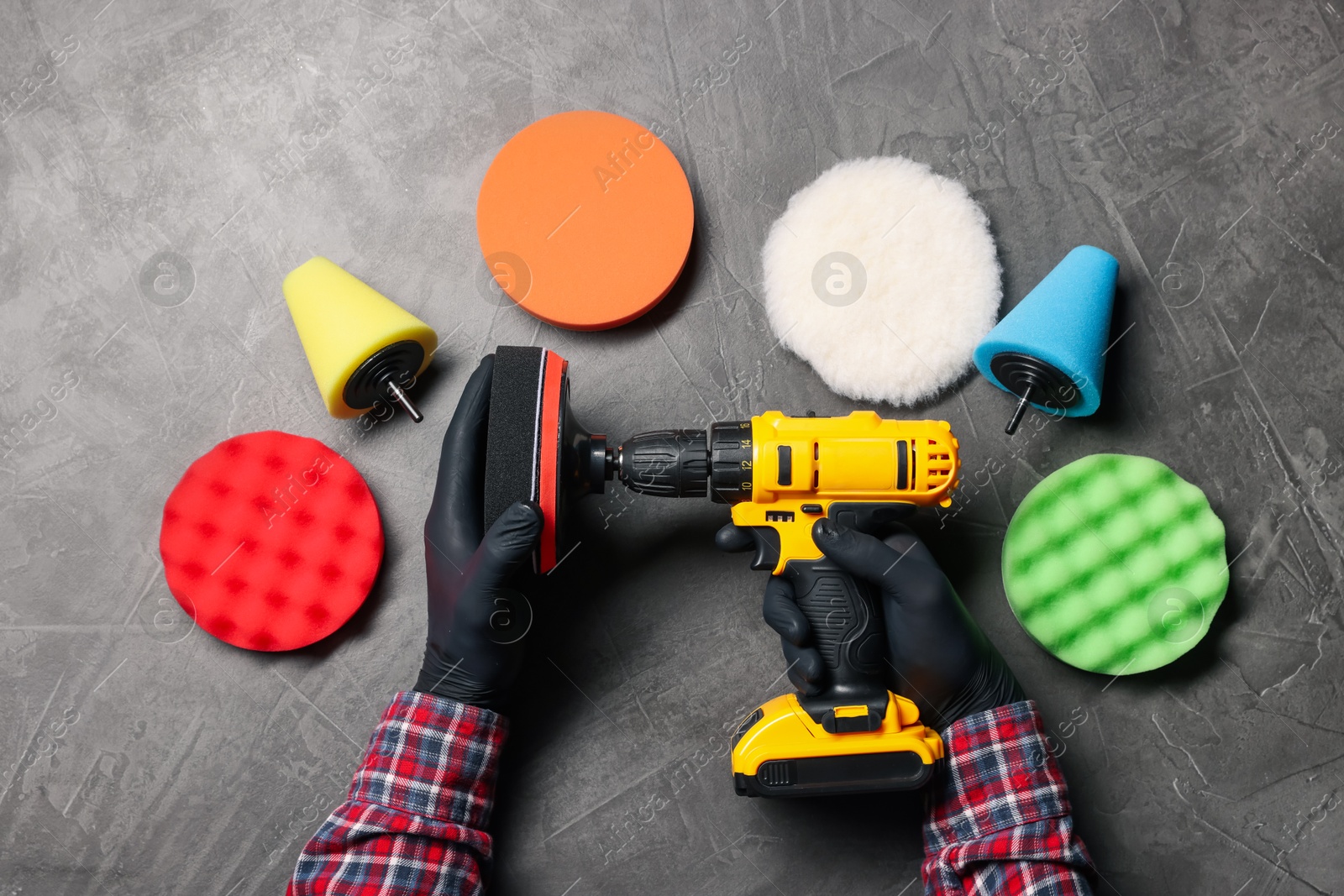 Photo of Man holding electric screwdriver with polish pad among colorful ones at grey textured table, top view