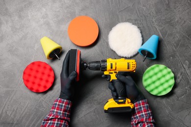 Photo of Man holding electric screwdriver with polish pad among colorful ones at grey textured table, top view