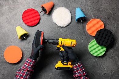 Photo of Man holding electric screwdriver with polish pad among colorful ones at grey textured table, top view