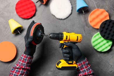 Photo of Man attaching polish pad onto electric screwdriver among colorful ones at grey textured table, top view