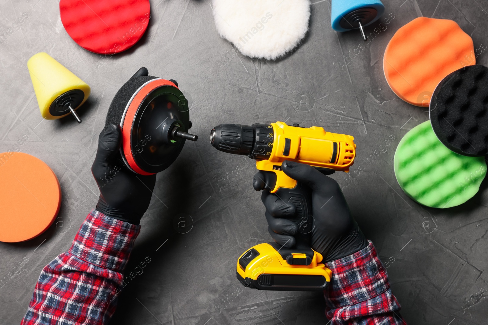 Photo of Man attaching polish pad onto electric screwdriver among colorful ones at grey textured table, top view