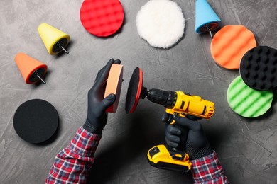 Photo of Man attaching polish pad onto electric screwdriver among colorful ones at grey textured table, top view