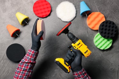 Photo of Man attaching polish pad onto electric screwdriver among colorful ones at grey textured table, top view