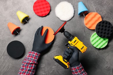 Photo of Man holding electric screwdriver among polish pads at grey textured table, top view