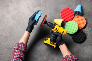 Photo of Man attaching polish pad onto electric screwdriver among colorful ones at grey textured table, top view