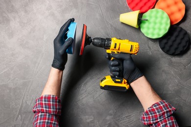 Photo of Man attaching polish pad onto electric screwdriver among colorful ones at grey textured table, top view