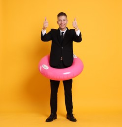 Photo of Businessman with inflatable ring showing thumbs up on orange background