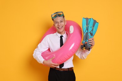 Photo of Businessman with inflatable ring, flippers and diving mask on orange background