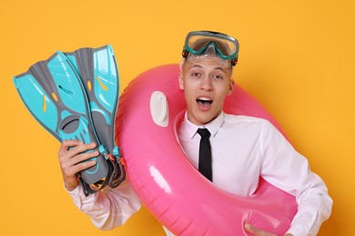 Photo of Businessman with inflatable ring, flippers and diving mask on orange background