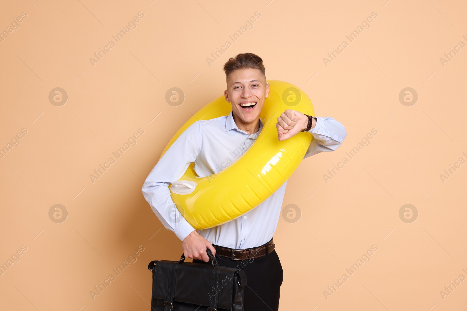 Photo of Businessman with inflatable ring and briefcase checking time on beige background