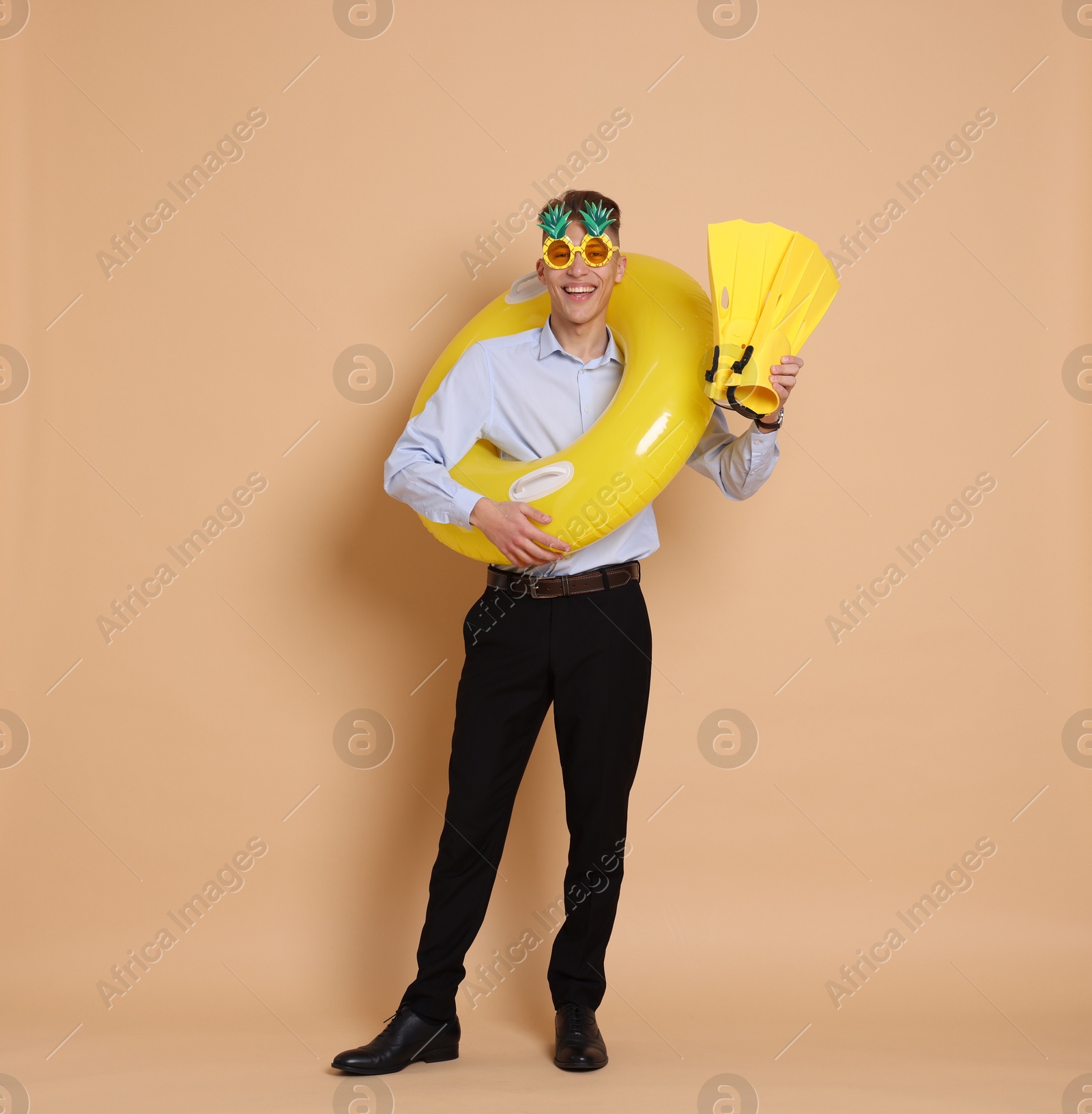 Photo of Businessman with inflatable ring, funny sunglasses and flippers on beige background