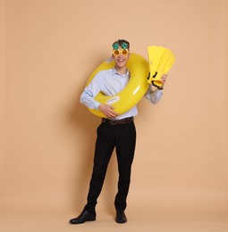 Photo of Businessman with inflatable ring, funny sunglasses and flippers on beige background