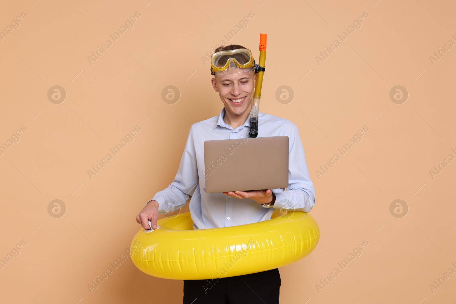 Photo of Businessman with inflatable ring, laptop and snorkeling equipment on beige background