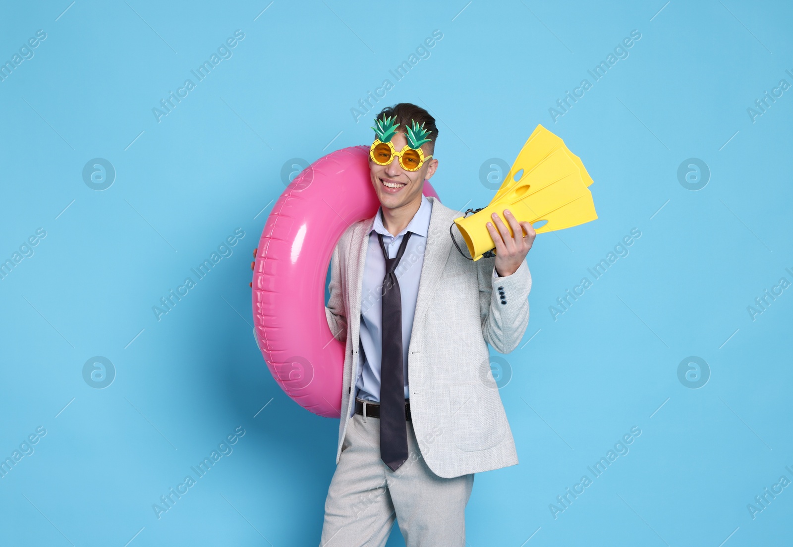 Photo of Businessman with inflatable ring, funny sunglasses and flippers on light blue background