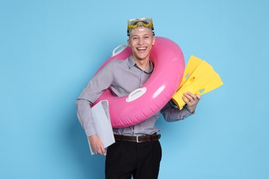 Photo of Businessman with inflatable ring, flippers, folder and diving mask on light blue background