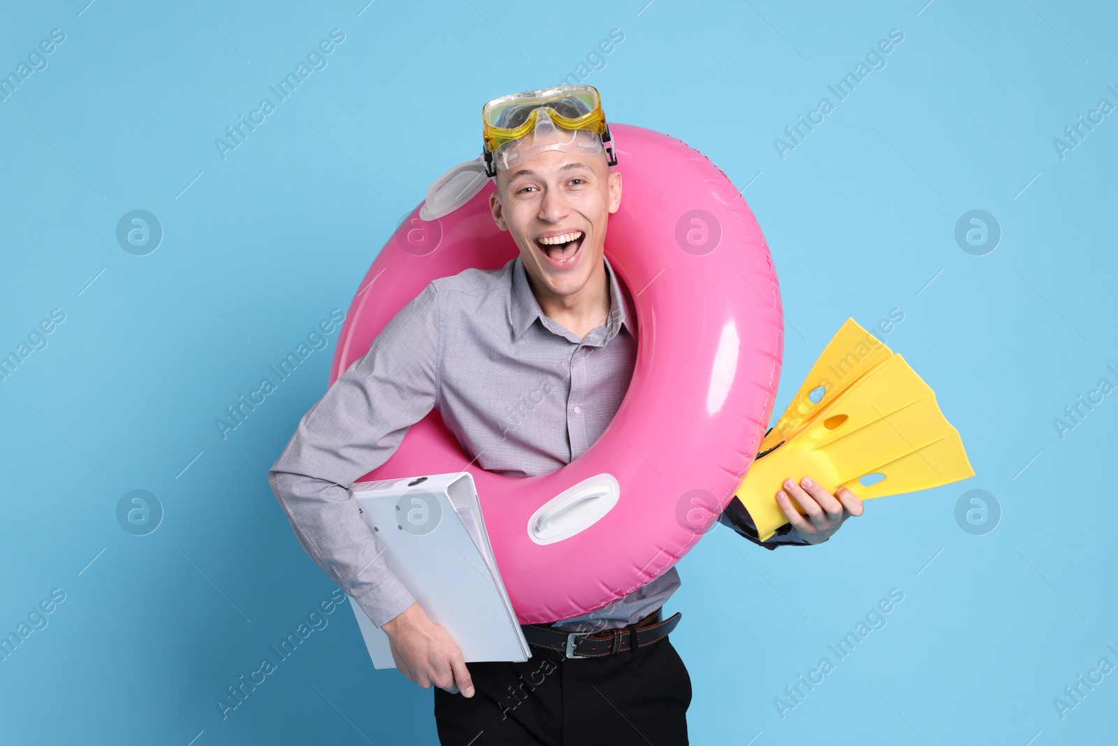 Photo of Businessman with inflatable ring, flippers, folder and diving mask on light blue background