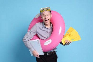 Photo of Businessman with inflatable ring, flippers, folder and diving mask on light blue background