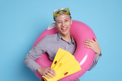 Photo of Businessman with inflatable ring, flippers and diving mask on light blue background