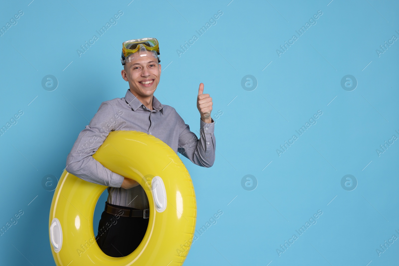 Photo of Businessman with inflatable ring and diving mask showing thumbs up on light blue background, space for text