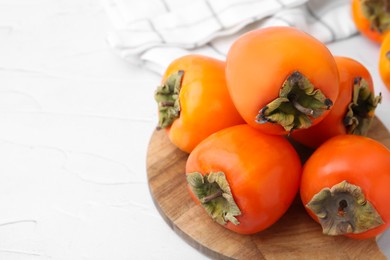 Photo of Delicious fresh juicy persimmons on white table, closeup. Space for text