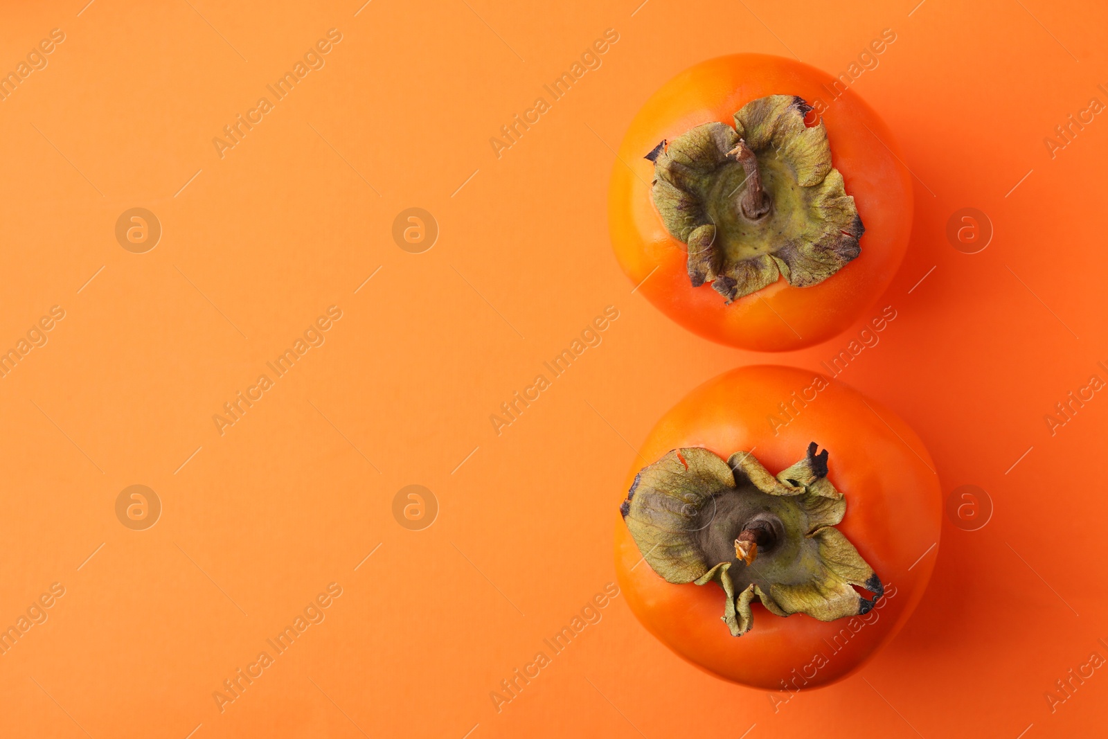 Photo of Delicious fresh juicy persimmons on orange table, flat lay. Space for text