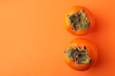 Delicious fresh juicy persimmons on orange table, flat lay. Space for text