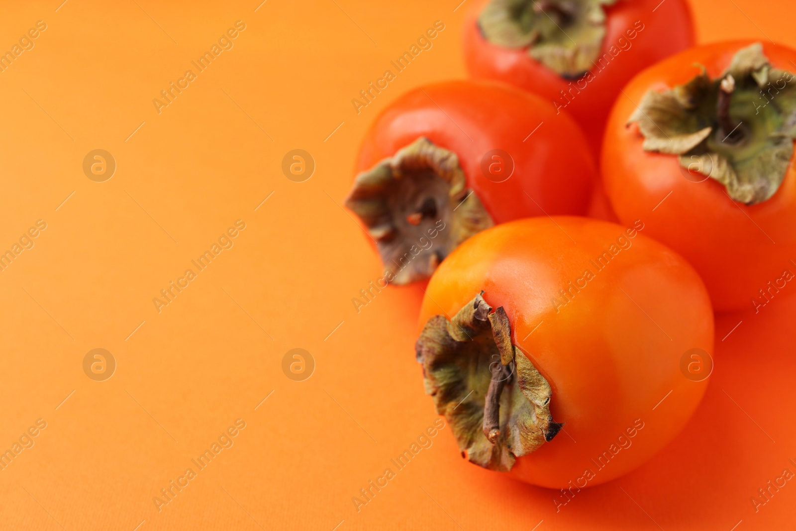 Photo of Delicious fresh juicy persimmons on orange table, closeup. Space for text