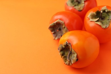 Photo of Delicious fresh juicy persimmons on orange table, closeup. Space for text