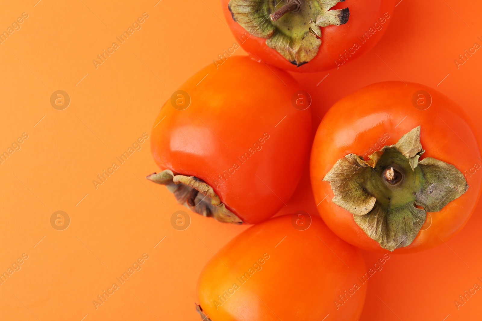 Photo of Delicious fresh juicy persimmons on orange table, flat lay. Space for text