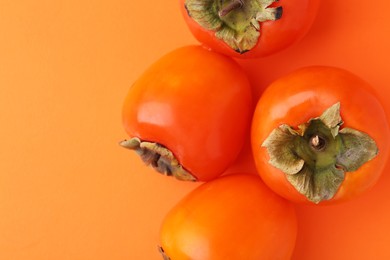 Delicious fresh juicy persimmons on orange table, flat lay. Space for text